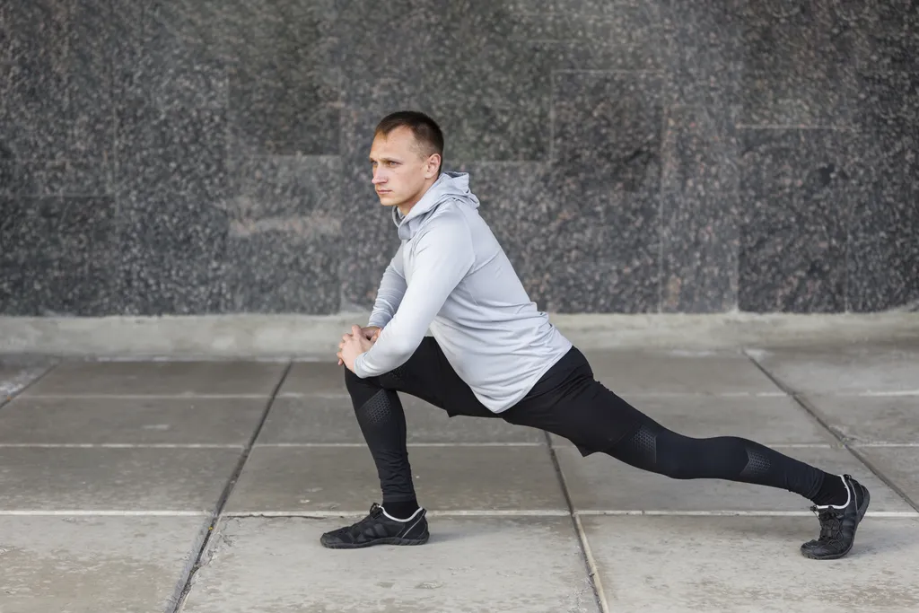 Athletic man performing a lunge stretch outdoors in sportswear